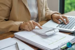 Person using a calculator and laptop during a financial checkup.