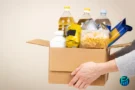 Person holding a cardboard box filled with essential groceries, illustrating a helpful step for those researching how to find a food pantry.